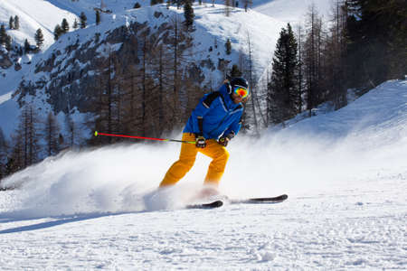 Male skier in blue and yellow clothes on slope with mountains in the background at Cortina d'Ampezzo Faloria skiing resort area Dolomiti Italyの写真素材