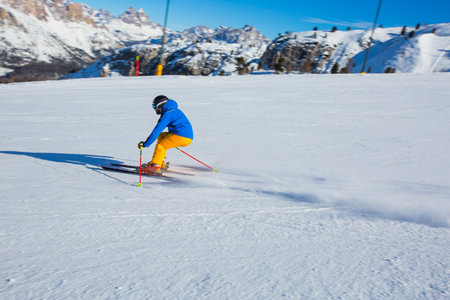 Male skier in blue and yellow clothes on slope with mountains in the background at Cortina d'Ampezzo Faloria skiing resort area Dolomiti Italyの写真素材