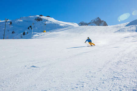 Male skier in blue and yellow clothes on slope with mountains in the background at Cortina d'Ampezzo Faloria skiing resort area Dolomiti Italyの写真素材