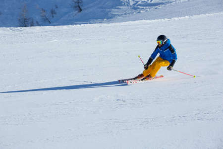 Male skier in blue and yellow clothes on slope with mountains in the background at Cortina d'Ampezzo Faloria skiing resort area Dolomiti Italyの写真素材
