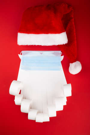 Santa Claus beard hat with face mask on red background, creative minimal concept of Christmas and New Year safe celebrationの写真素材