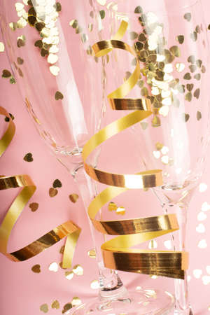 Valentines day champagne flutes glasses and heart shaped gold glitters on pink backgroundの写真素材