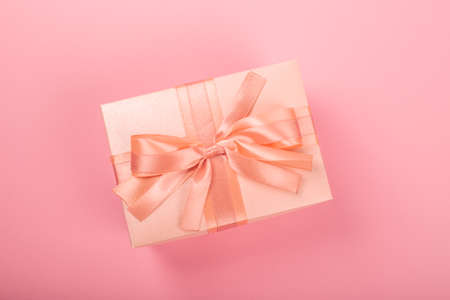 Valentines Day gift in a box wrapped in striped paper and tied with silk ribbon bow on pink background with copy space for textの写真素材