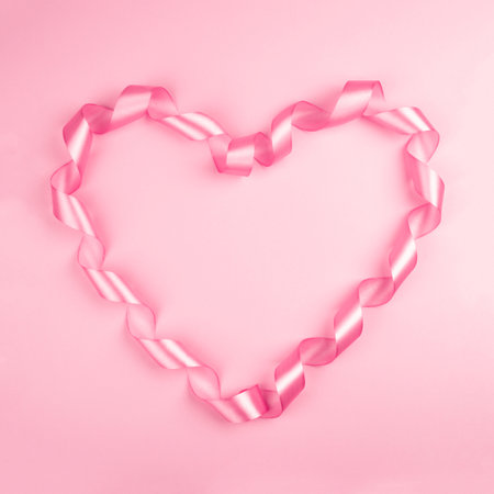 Valentine day background with pink curly satin ribbon in heart shape on paper on with copy space for textの写真素材