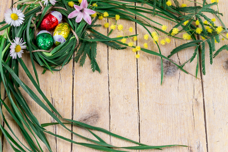Decorative composition of mimosa, flowers and chocolate eggs for Easter on wooden backgroundの写真素材