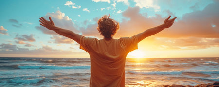 Man with raised hands standing on the beach and looking at the sunsetの素材
