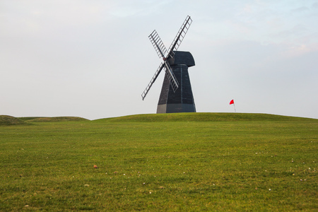 Windmill and red flag with green lawn and overcast sky in Rottingdean Windmill golf course. East Sussex, England.の写真素材