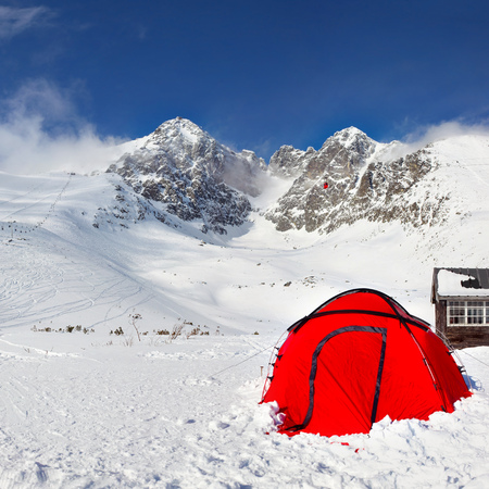 Bright red climbing tent on snow with Lomnicky Stit peak in the background, on a sunny winter day. Tatranska Lomnica ski resort, Slovakiaの写真素材
