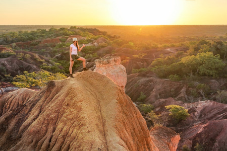 Young woman standing on top of the hill, pointing at the sun during sunset, Marafa (Hell kitchen), Kenya.の写真素材