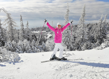 Young woman in pink ski jacket with skis on her feet holding ski poles up, in happy pose smiling during nice sunny winter day. Strbske pleso ski resort, Slovakia.
の写真素材