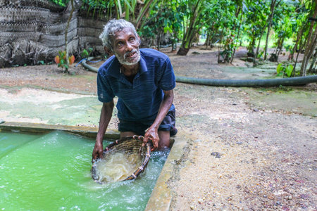 Galle, Sri Lanka - April 14, 2017: Local man knee deep in hole full of water showing tourists how moonstones (semi precious gems) are extracted in moonstone mine.のeditorial素材