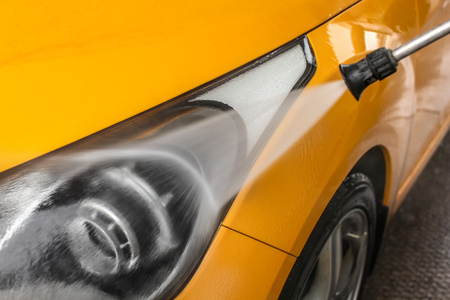 Detail on dark yellow car front light being washed with jet water spray in carwash.の写真素材