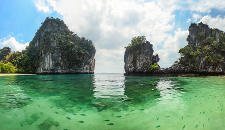 Panorama of sharp karst cliffs rising from water with clear green sea full of fish in foreground. Hong Islands, Thailandの写真素材