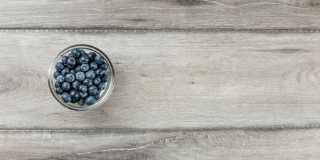 Wide shot from above to small glass cup full of blueberries on gray wood desk, with space for text.の写真素材