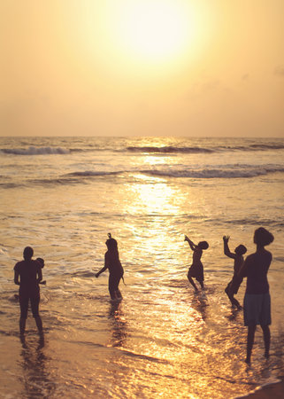 Kalutara, Sri Lanka - April 15, 2017: Silhouettes of people, mostly children playing on the beach in the sea in golden sunset evening light.のeditorial素材