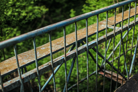 Old metal guard rail of bridge, with blurred green forest in background.の写真素材