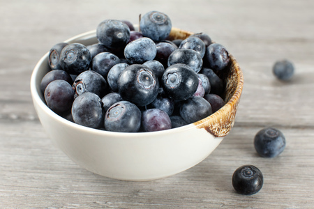 Small bowl full of blueberries, some of them spilled on gray wood desk.の写真素材