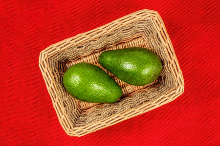 Table top view on two whole avocado fruits in basket, with red tablecloth under it.の写真素材