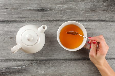 Table top view - woman hand holding spoon, stirring tea in white porcelain cup.の写真素材