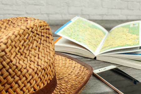Straw hat, guide book with map, and mobile phone on gray wood desk. Travel planning concept.の写真素材