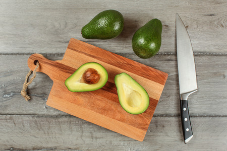 Table top view - avocado cut in half on wooden chopping board, chef knife next to it, two whole green pears above.の写真素材