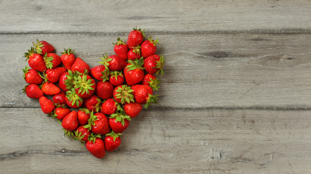 Tabletop view, strawberries on wood desk, arranged in shape of heart, space for text right.の写真素材