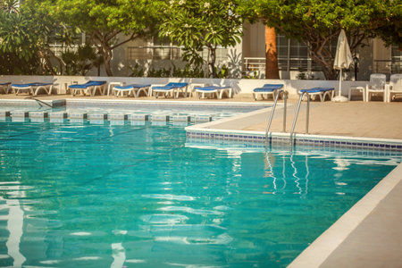 Empty hotel resort swimming pool, lit by morning sun, few leaves on the water surfaceのeditorial素材