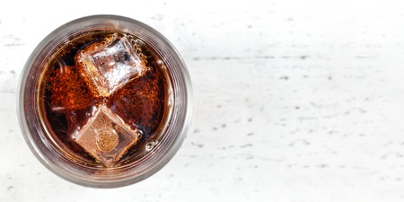 Tabletop view, glass with cola drink and ice cubes on white board. Wide photo, space for text right.の写真素材