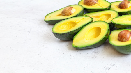 Halved avocados fruits with green yellow pulp, some brown seeds visible on white working board -...