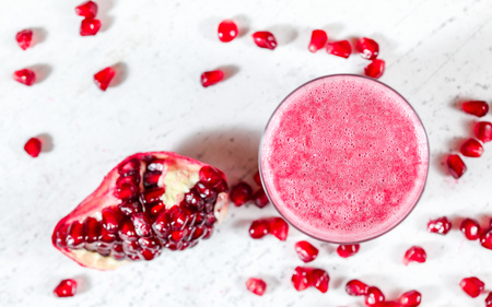Pomegranate smoothie with blurred gem like fruits scattered near on white board. Photo from above, focus on bubbles in drink foamの写真素材