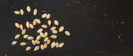 Roasted, salted pumpkin seeds on black marble like working board, photo from above, wide banner with...