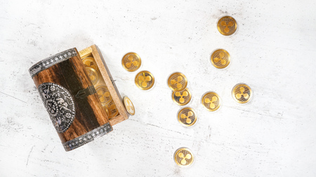 Small wooden decorated chest with XRP ripple cryptocurrency golden coins, some scattered on white stone board, photo from aboveの写真素材