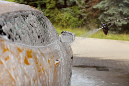 Side and side mirror of yellow car being washed in self service carwash, foam and shampoo spraying, drops in the air.の写真素材
