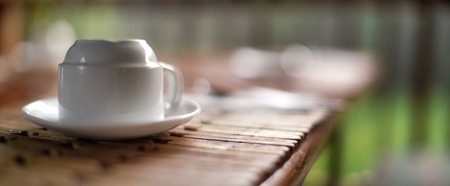 Empty white porcelain cup, upside down, on wooden table, blurred green background. Very shallow depth of field photo - only edges and few wood boards in focus, space for text right.の写真素材