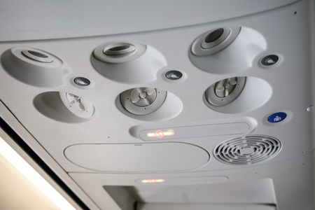 Air conditioning vents, lights and buttons on ceiling of airplane above passenger seat, no smoking sign is lit.の写真素材