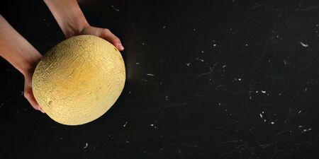 Top down view, woman hands holding cantaloupe melon over black marble like board. Wide banner with space for text on right sideの写真素材