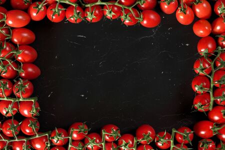 Group of cherry tomatoes on black marble like board, arranged in frame around, rectangular space for text in middleの写真素材