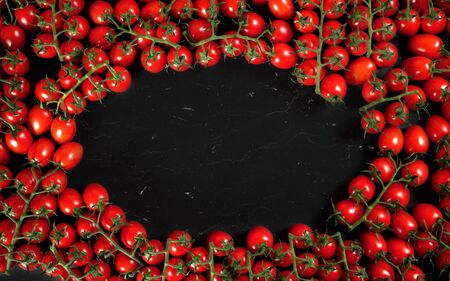 Top down view, heap of cherry tomatoes with green vine leaves arranged in circle frame on black marble like board, space for text at middleの写真素材