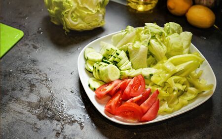 Cut tomatoes, cucumber and iceberg salad on dark kitchen board