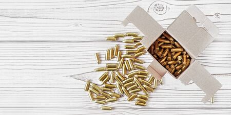 Top down view, carton box with yellow brass ammunition bullets on white wooden desk, banner - space for text left sideの写真素材