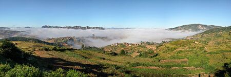 High resolution panorama - typical Madagascar landscape at Alakamisy Ambohimaha region fog rolls over green valley with terraced rice field, clay houses on small hills, higher mountains in backgroundの写真素材