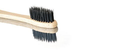 Wooden bamboo toothbrush with black bristles, closeup detail isolated on glossy white table...