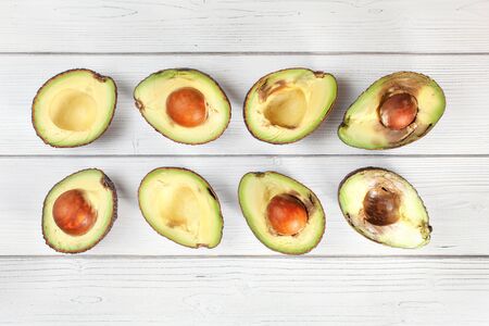 Avocado halves on white boards desk, view from above. Fruits arranged from unripe to overripe.