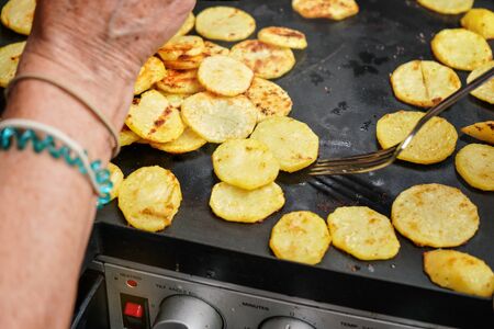 Potato cut to thin circles grilled on electric grill, fork and senior woman hands over food.の写真素材
