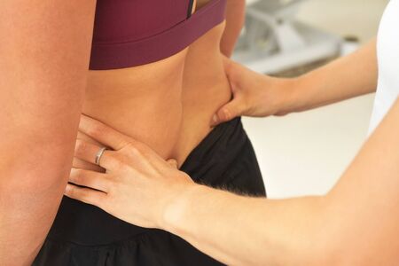 Woman patient at physiotherapy session, detail on therapist hands touching muscles on her back.