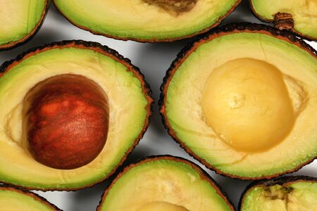 Avocado halves, one fruit with brown seed inside, arranged on white board, closeup macro detail.の写真素材