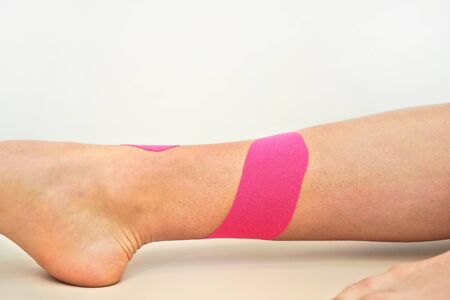 Pink kinesiology tape applied over lower leg and ankle of young female, closeup detail.の写真素材