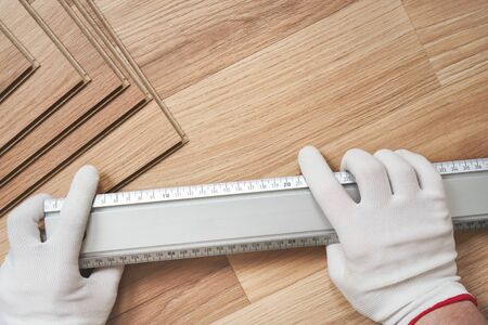 Installing laminated floor, detail on man hands in white gloves holding metal ruler over wooden tile, view form above.の写真素材