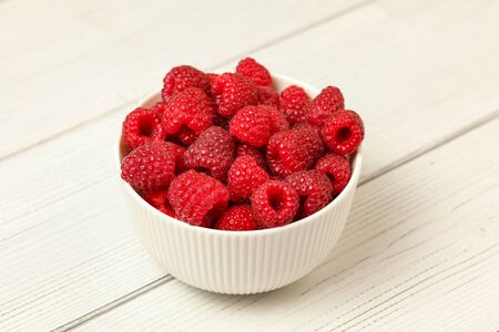 Small porcelain cup with raspberries on white boards desk.