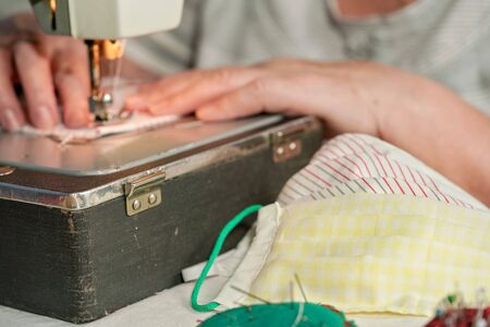 Elderly senior woman working on old sewing machine - making home made face masks against coronavirus spreading, closeup focus detail to finished masks in foregroundの写真素材